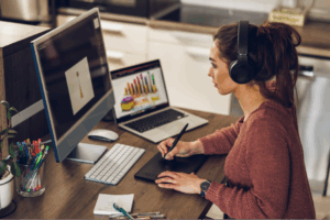 Mulher estudando marketing odontológico e tomando notas em frente a um desktop e laptop.